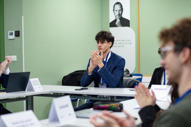 A delegate in a navy suit applauds during a committee session.