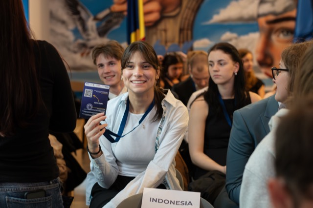 The smiling delegate of Indonesia holds her badge up toward the camera.