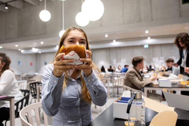 A delegate playfully holds a burger in front of her face in the cafeteria.