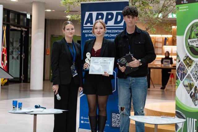 An awardee holds her certificate and spiral trophy between two presenters.