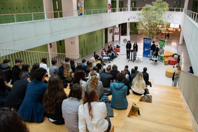Overhead view of the school atrium with delegates on wooden steps watching the closing ceremony.